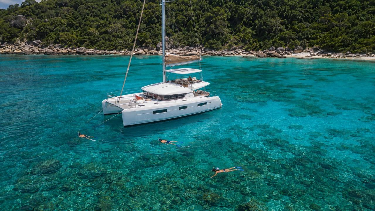 Catamaran anchored over a reef at Racha Yai with three snorkelers in clear turquoise water